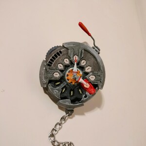 May include: A silver and red metal gear with a chain attached. The gear has a red lever and a small orange gear in the centre.