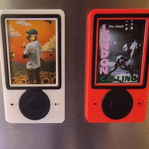 May include: Two decorative magnets resembling music players. One is white with a picture of a person in a field of sunflowers. The other is red with the words "LONDON CALLING" and a band image.