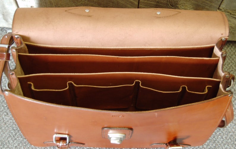 May include: A brown leather briefcase with multiple compartments and pockets. The briefcase has a flap closure with a metal buckle.