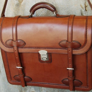 May include: A brown leather briefcase with a metal clasp and a shoulder strap. The briefcase has decorative stitching and buckles.