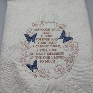 Puede incluir: Tela acolchada blanca con texto bordado que dice "Aunque tu sonrisa se ha ido para siempre y no puedo tocar tu mano, todavía tengo tantos recuerdos de la persona que tanto amé". El bordado es de color rosa y presenta dos mariposas azules.