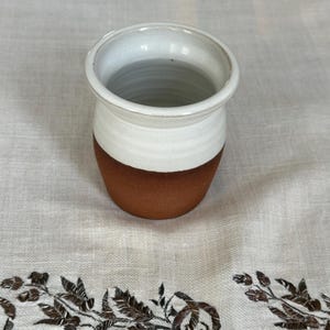 May include: A white ceramic vase with a brown base. The vase is round and has a wide opening.