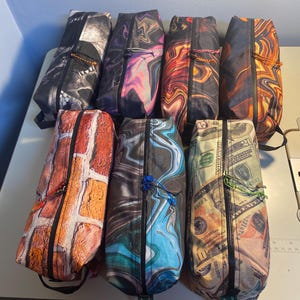 Peut inclure: Huit pochettes zippées différentes avec divers motifs colorés et abstraits. Les motifs comprennent un crâne, un motif de briques, des motifs marbrés et un imprimé argent.