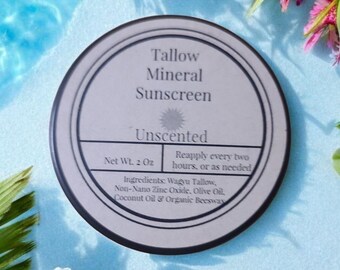 Op de afbeelding: Een witte ronde container met een zwart label waarop "Tallow Mineral Sunscreen Unscented" en "Net Wt. 2 Oz" staat. Het label bevat ook instructies om elke twee uur of indien nodig opnieuw aan te brengen en vermeldt de ingrediënten: Wagyu Tallow, Non-Nano Zinc Oxide, Olijfolie, Kokosnootolie & Biologische Bijenwas.