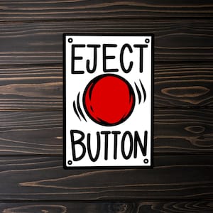 May include: A white sign with black lettering that reads "EJECT BUTTON" with a large red circle in the center.