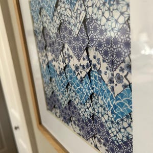 Könnte beinhalten: Ein gerahmtes Kunstwerk mit einem geometrischen Muster aus blauem und weißem Origami-Papier. Das Papier ist in einem sich wiederholenden Muster aus überlappenden Quadraten und Dreiecken angeordnet.
