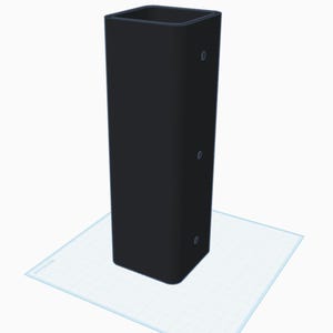 May include: A tall, black, rectangular container with rounded corners. The container has three small, circular indentations on one side. It is placed on a light blue, grid-patterned surface.