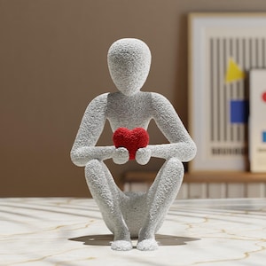 May include: A white, textured, abstract sculpture of a person sitting with their legs crossed and holding a red heart in their hands.