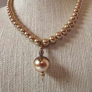 May include: A gold pearl necklace with a large, round, gold pearl pendant.