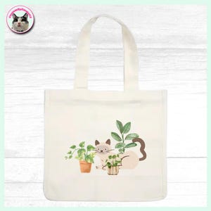 Puede incluir: Bolso tote de color crema con una ilustración de acuarela de un gato y plantas. El gato es de color marrón claro con detalles en marrón oscuro, y las plantas están en macetas de terracota. El bolso tiene un diseño sencillo con un asa.
