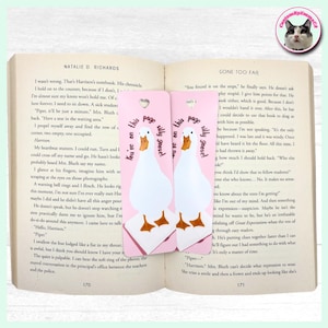 May include: Two pink bookmarks featuring a white goose design and the text "You're on this page silly goose!". The bookmarks are placed in an open book.