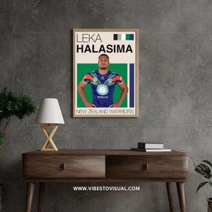 Puede incluir: Un póster enmarcado con Leka Halasima con la camiseta de los New Zealand Warriors. El póster tiene un fondo beige con el nombre del jugador y el logotipo del equipo. La camiseta es azul, verde y roja. El póster se muestra en una mesa de madera.