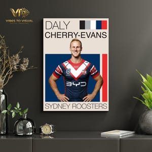 May include: A framed poster featuring a rugby player in a navy blue, red, and white jersey. The poster includes the player's name, "DALY CHERRY-EVANS," and the team name, "SYDNEY ROOSTERS," with a color palette at the top.