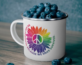 May include: White enamel mug with a rainbow sunflower design and a peace sign in the center. The text around the sunflower reads "We are powerful because we have survived."