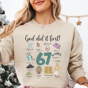 May include: A beige sweatshirt featuring the phrase "God did it first!" alongside colourful illustrations and Bible verses. The sweatshirt is worn with red and white plaid pyjama bottoms. A white mug with a Santa Claus design is held.