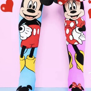 May include: A pair of knee-high socks featuring Mickey Mouse and Minnie Mouse. The Mickey Mouse sock is blue with a red and yellow Mickey Mouse design. The Minnie Mouse sock is pink with a red and white Minnie Mouse design. Both socks have 3D ears.