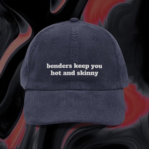 May include: Navy blue corduroy baseball cap with the text "benders keep you hot and skinny" in white. The cap has a curved brim and a fabric-covered adjustable strap at the back. The hat is a casual accessory.