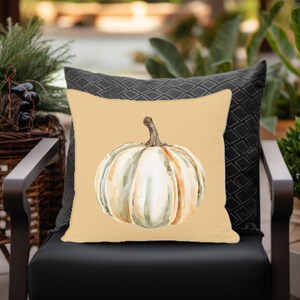 May include: A beige throw pillow with a watercolor illustration of a white pumpkin with brown and green accents.