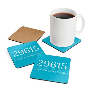 Op de afbeelding: Twee turquoise blauwe onderzetters met de tekst "29615 Greenville, South Carolina" erop. Een bruine kurken onderzetter is op de achtergrond. Een witte mok met koffie staat op een turquoise blauwe onderzetter.