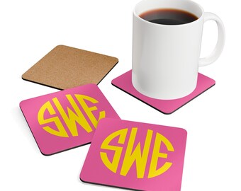 May include: Four pink coasters with a yellow monogram "SWE" in a circle. One coaster is under a white coffee mug with coffee inside.