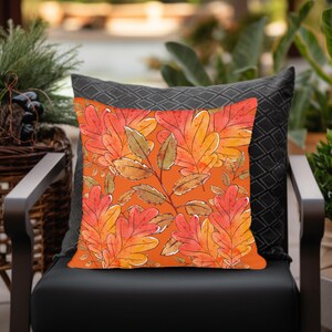 May include: Orange throw pillow with a watercolor pattern of autumn leaves. The leaves are in shades of orange, red, and yellow.