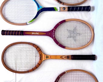 May include: Five vintage wooden tennis rackets with various handle and frame designs. The rackets feature different brand names, including Wilson, Spalding, and Davis. The rackets have a natural wood finish with dark brown and black grips and stringing.