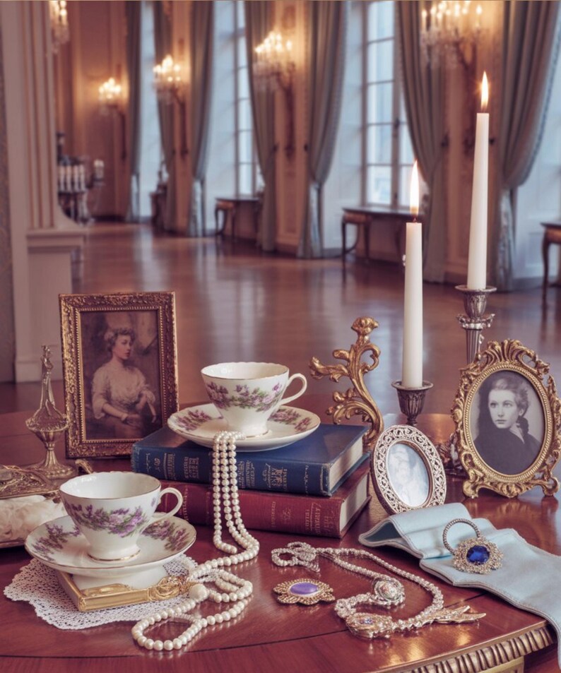 May include: A vintage-themed still life featuring a table adorned with antique items. Two teacups and saucers with floral designs sit atop books. Pearl necklaces, framed portraits, and lit candles add to the elegant ambiance. A gold-framed picture and jewelry are also present.