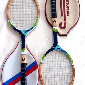 May include: Two vintage Chemold tennis rackets with wooden frames and white mesh. One racket has a blue, green, and white handle with the word "Signature" on it. The other racket has a matching design. Both rackets have matching cases.