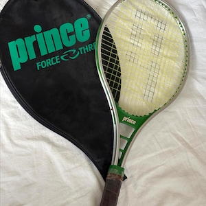 May include: A green and silver Prince tennis racket with a black racket cover. The racket has yellow strings and a brown grip. The racket cover has the word "Prince" in large green letters.