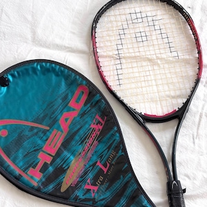 May include: A black and red HEAD tennis racket with a white string net and a black grip. A teal and black racket cover with the HEAD logo and "Xtra Long" text is next to the racket. The racket and cover are on a white surface.
