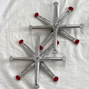 May include: Two silver Zephyr brand wheel alignment tools with red tips, arranged on a white fabric surface. Each tool has a star-like design with multiple arms extending from a central hub. The tools are designed for automotive use.