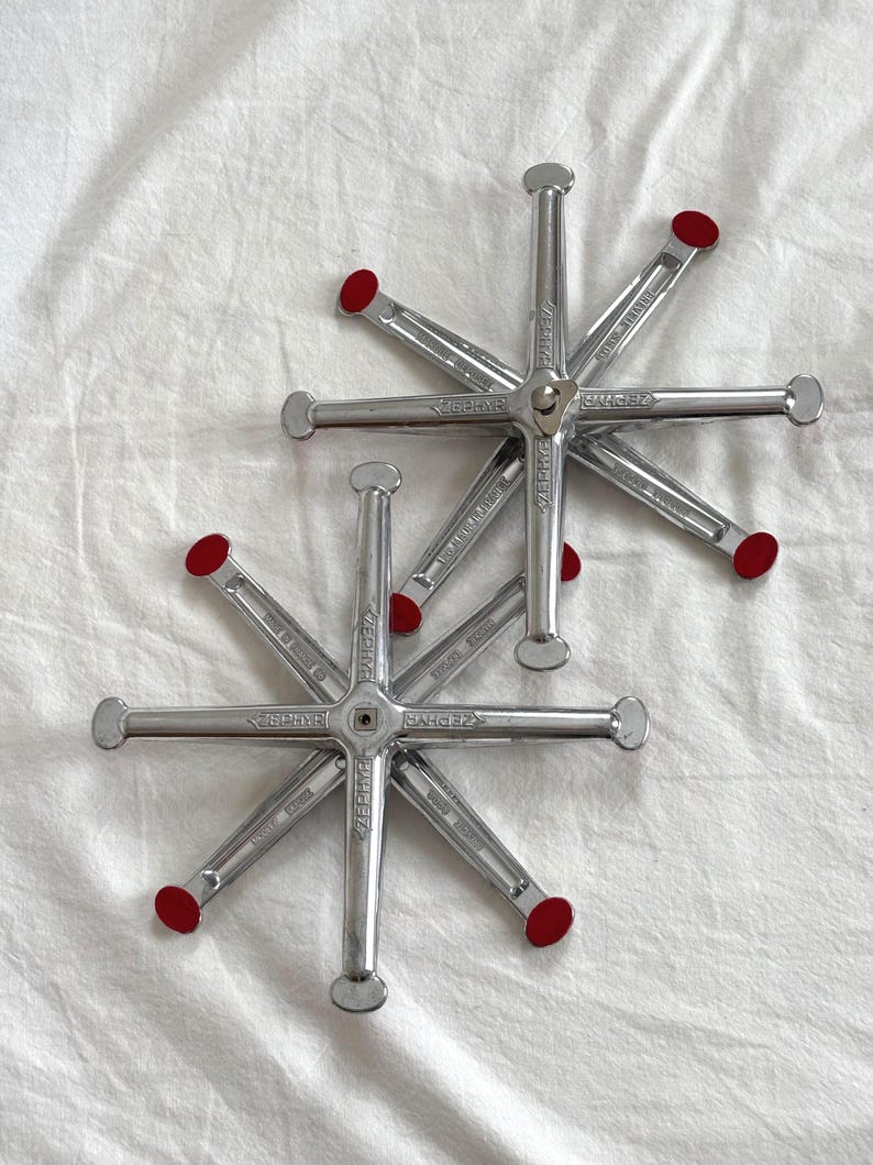 May include: Two silver Zephyr brand wheel alignment tools with red tips, arranged on a white fabric surface. Each tool has a star-like design with multiple arms extending from a central hub. The tools are designed for automotive use.