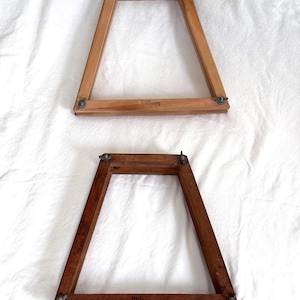 May include: Two vintage wooden tennis racket frames. The frames are trapezoidal, with rounded corners and metal hardware. The frames are different shades of brown, and the word "Wilson" is printed on the bottom of each frame.