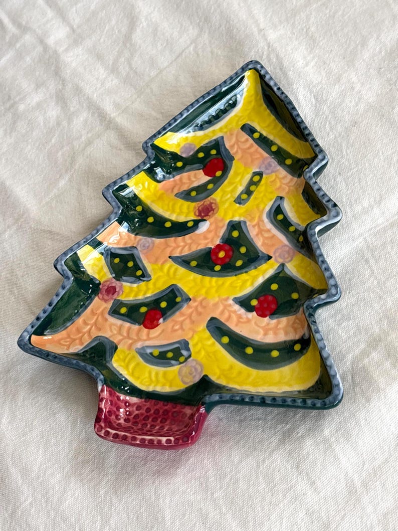 May include: A ceramic Christmas tree-shaped plate with a yellow and green design. The plate has a red base and is decorated with red and yellow dots. The edges are outlined in dark green and blue.