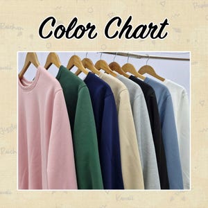 May include: A colour chart showing a range of crewneck sweatshirts in various colours. The sweatshirts are suspended on wooden hangers. Colours include pink, green, navy, beige, grey, black, light blue, and white. The text "Color Chart" is at the top.