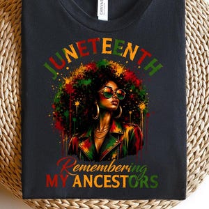 Könnte beinhalten: Schwarzes T-Shirt mit einem farbenfrohen Grafikdesign einer Frau mit Afro, Sonnenbrille und Jacke. Der Text "Juneteenth" steht über dem Bild, darunter "Remembering My Ancestors". Das Design verwendet rote, grüne und gelbe Farbtöne.