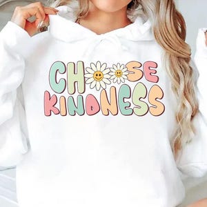 May include: White hoodie with the words "CHOOSE KINDNESS" in pastel colors and daisy accents. The hoodie is a casual garment, perfect for everyday wear.