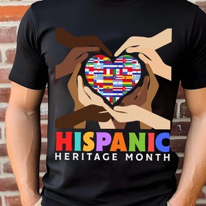 May include: Black t-shirt featuring a heart-shaped design composed of various flags, surrounded by hands of different skin tones. The text "HISPANIC HERITAGE MONTH" is displayed in colorful letters below the heart.
