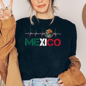 May include: Black t-shirt with the word "MEXICO" in green, white, and red, and a heartbeat line design. The shirt also features the Mexican coat of arms. A casual top for those who love Mexico.