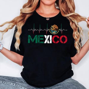 May include: Black t-shirt with the word "MEXICO" in green, white, and red, and a heartbeat line design above it. The Mexican coat of arms is on the right side of the heartbeat line.