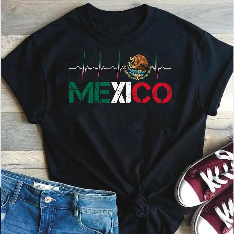 May include: Black t-shirt with the word "MEXICO" in green, white, and red, a heartbeat line design, and the Mexican coat of arms. The shirt is styled with blue jeans and burgundy trainers.