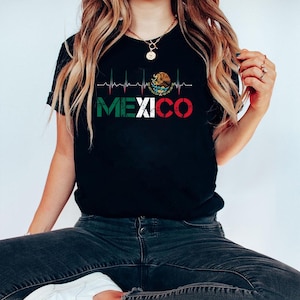 May include: Black t-shirt with the word "MEXICO" in white, green, and red, and a heartbeat graphic above. The design includes the Mexican coat of arms. The graphic is printed on the front of the shirt.