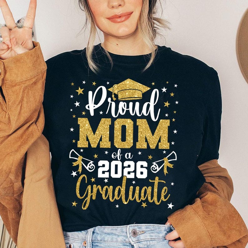 May include: Black t-shirt with the text "Proud MOM of a 2026 Graduate" in white and gold glitter lettering. The design includes a graduation cap, stars, and diploma illustrations. A perfect gift for a proud mother.