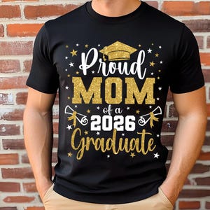 May include: Black t-shirt with a gold glitter design that reads "Proud MOM of a 2026 Graduate." The design includes a graduation cap, stars, and scrolls. The shirt is a crew neck and has short sleeves.
