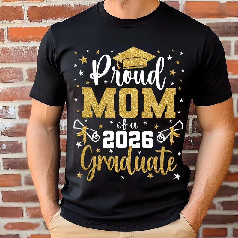 May include: Black t-shirt with a gold glitter design that reads "Proud MOM of a 2026 Graduate." The design includes a graduation cap, stars, and scrolls. The shirt is a crew neck and has short sleeves.