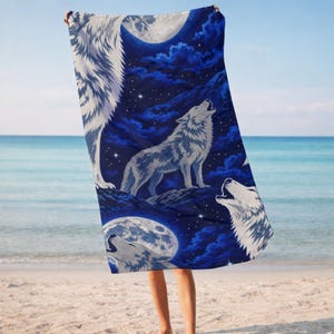 May include: A rectangular beach towel featuring a dark blue night sky background with multiple white wolves howling at a large, bright full moon. The design includes scattered white stars and deep blue clouds, creating a nocturnal scene.