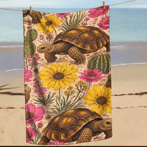 May include: A rectangular beach towel featuring a repeating pattern of brown tortoises, bright yellow sunflowers, pink wildflowers, and green cacti on a light tan background. The design covers the entire surface of the fabric.