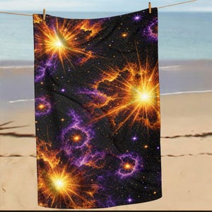 May include: A black beach towel with a vibrant cosmic design. The towel features bright orange and yellow bursts of light, surrounded by purple nebulas and scattered stars. It is hanging on a clothesline at the beach.