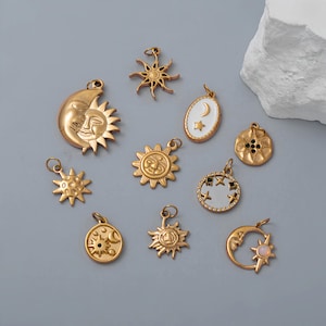Könnte beinhalten: Eine Sammlung goldfarbener Himmelscharms, darunter Sonnen, Monde und Sterne. Die Charms variieren im Design, einige zeigen detaillierte Gesichter und andere einfache Sternmuster. Einige Charms haben weißen Emaille und Kristallakzente.