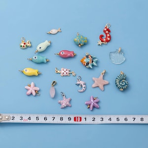 May include: A collection of colorful, nautical-themed charms, including fish, starfish, and seahorses. The charms are in various colors, such as blue, pink, and yellow. A ruler is placed below the charms, with measurements in inches.